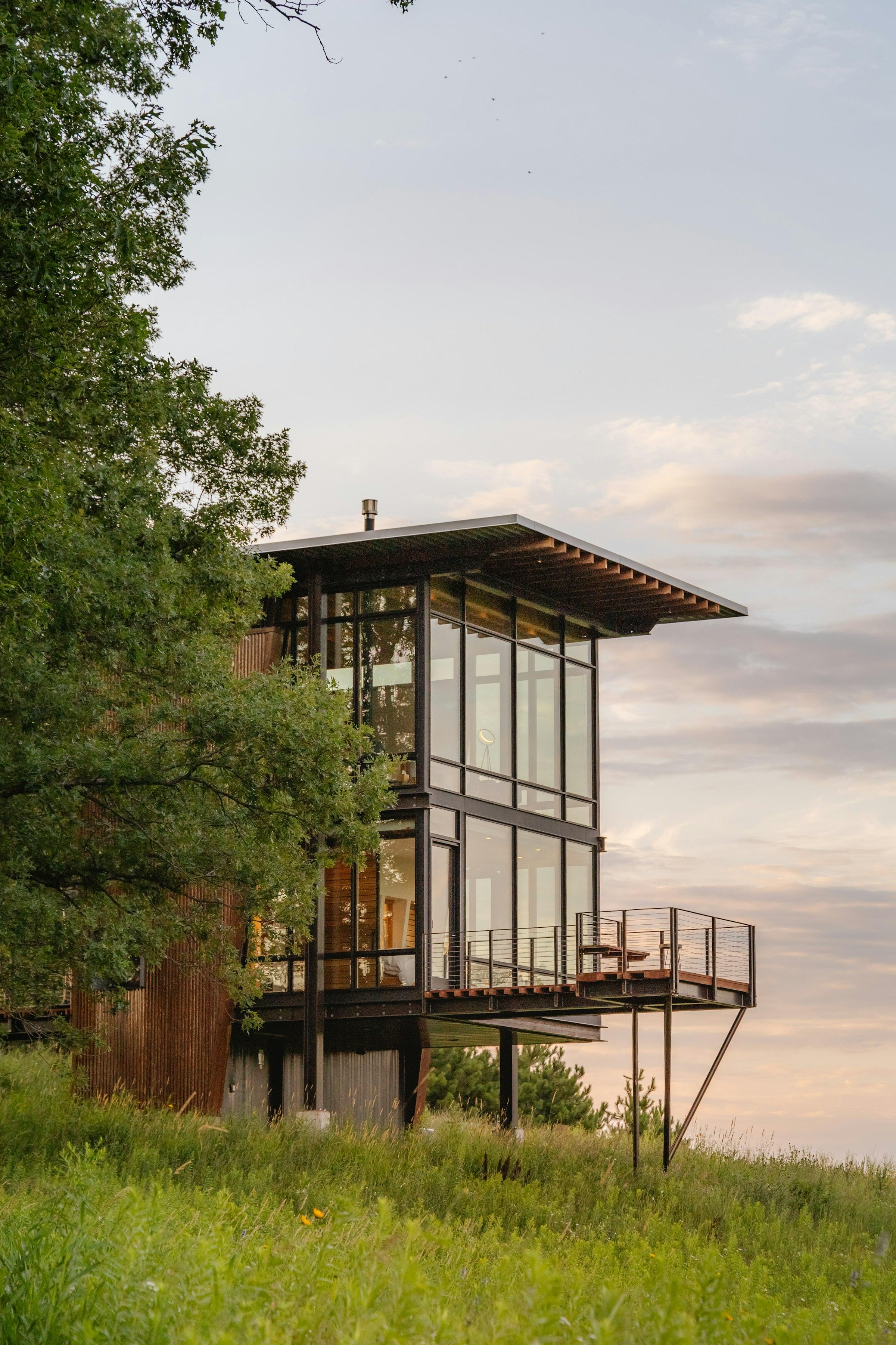 A glazed two-storey cabin on a steel frame at golden hour